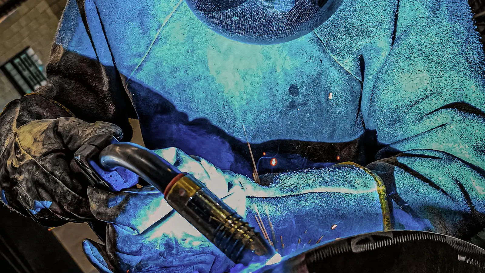 Welder in leathers and hood striking an arc