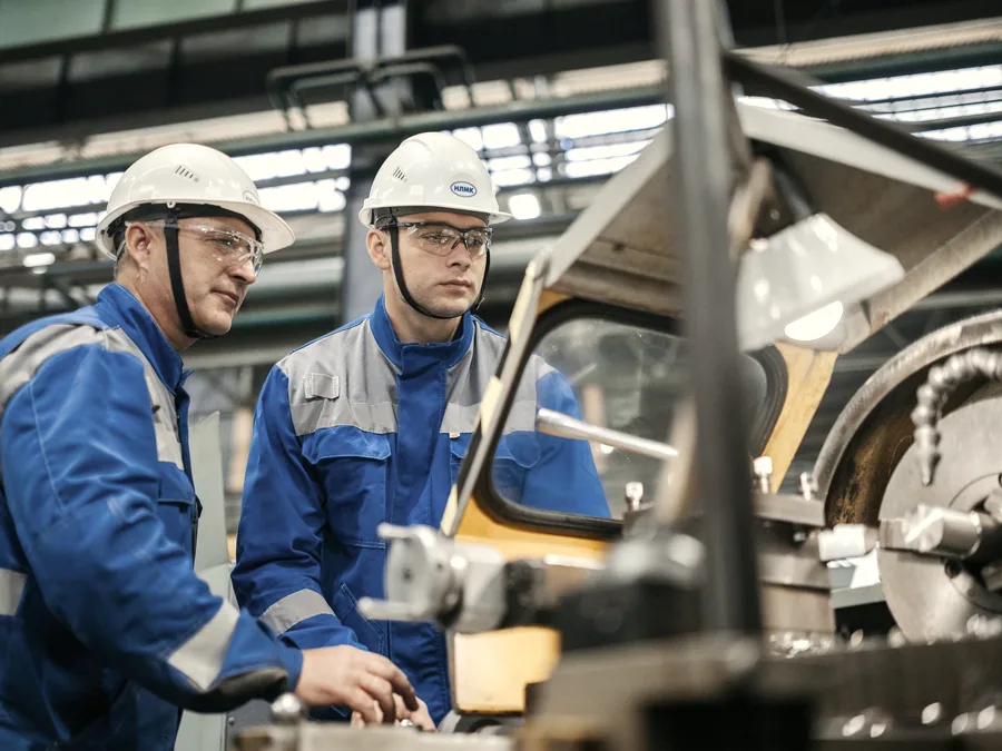 Two engineers in protective gear working on equipment in a workshop