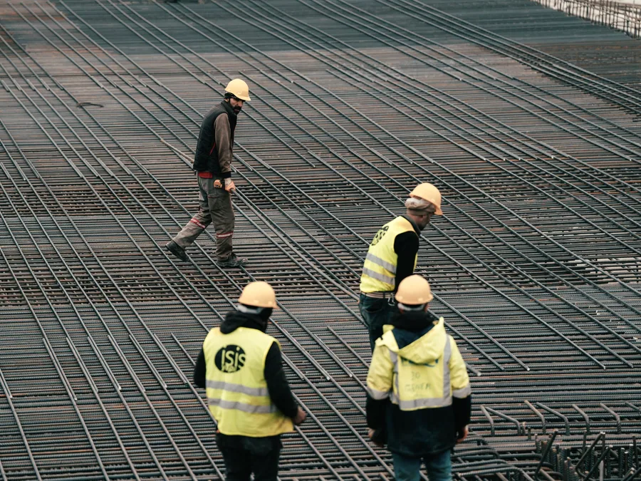 Steel fixers in hard hats and high visibility clothing working across a reinforcement mat