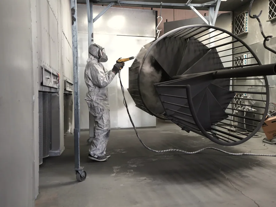 Worker in protective gear spray applying a coating to a large steel structure