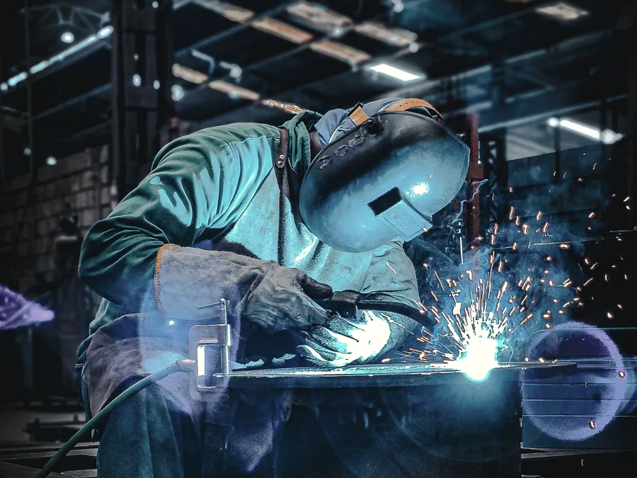 Welder in full helmet and gauntlets running a weld on steel